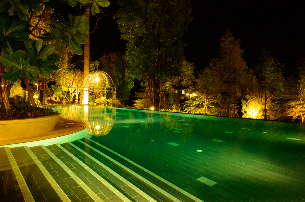 Piscine teinte en vert, la nuit, entourée de lumières diverses.