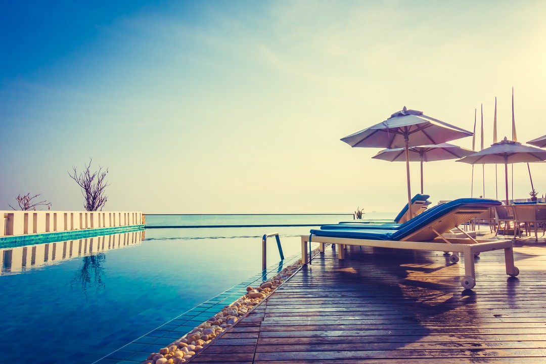 Transats en bois au bord d'une piscine au soleil couchant.